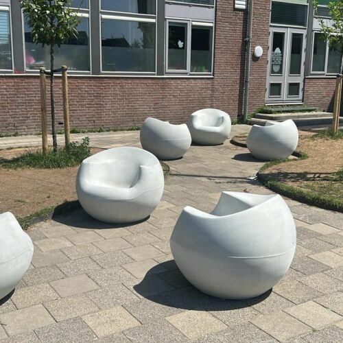 Betonnen zitelementen en tafel Stool 42 Drie witte design betonnen zitelementen uit de Stool collectie op een schoolplein